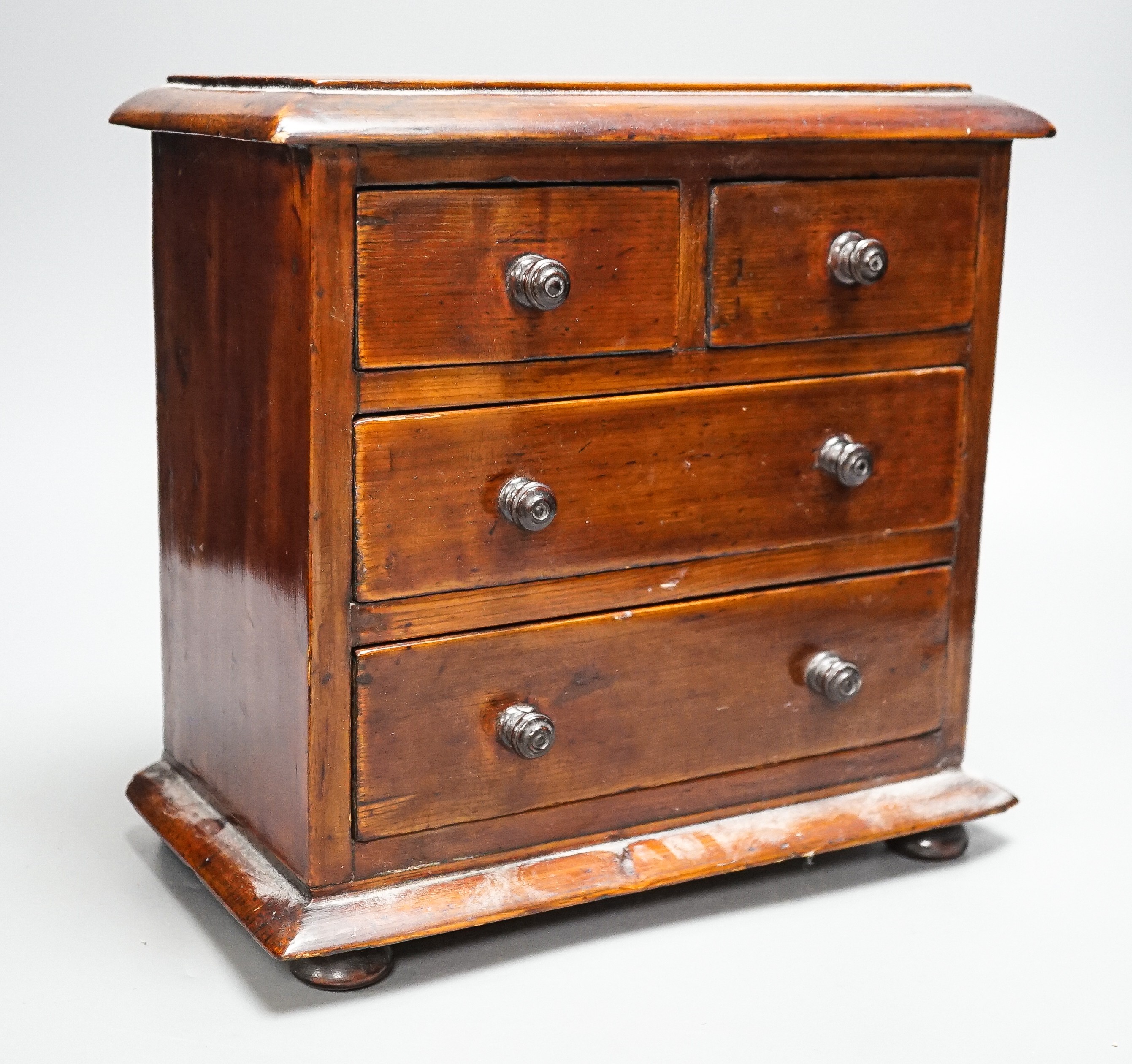 A Victorian stained pine miniature chest of drawers, 27 cms high.